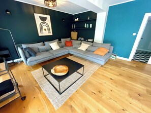 A modern living room with a sectional sofa, a coffee table, and a wall-mounted shelf with decorative items.