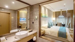 A modern hotel room with a large mirror, a round sink, a bed with a blue and white bedspread, and a television in the corner. - Ronghu Hotel (Yueyang County)