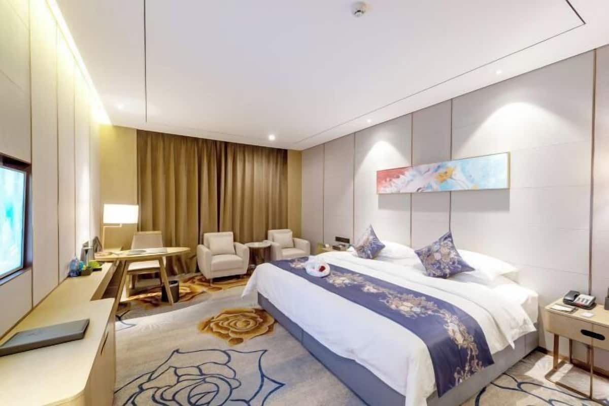 A hotel room with a large bed, a desk, a chair, a small table, and a TV.