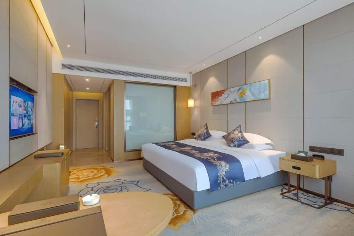 A modern hotel room with a large bed, a bedside table, a TV, and a bathroom with a glass door.