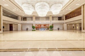 Un vestíbulo amplio con techo alto y candelabros, que cuenta con un mostrador de recepción central y plantas en macetas.