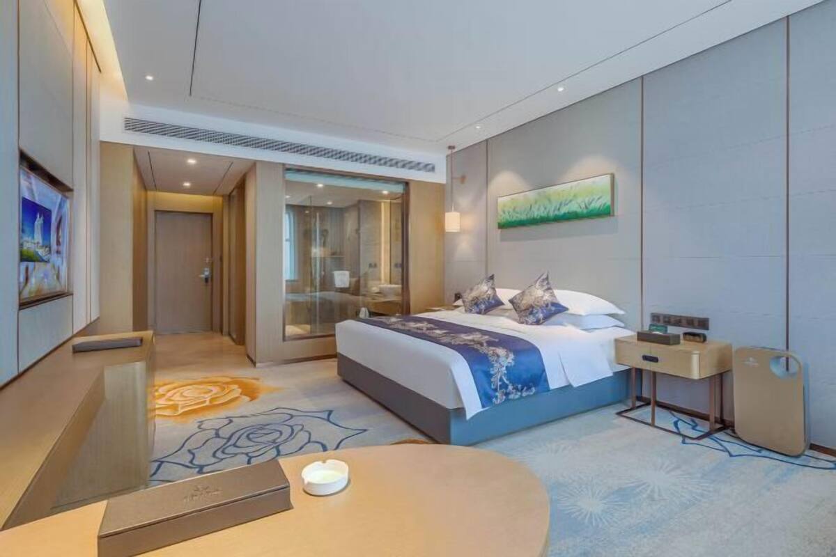 A modern hotel room with a bed, bedside table, and a glass-enclosed shower area.