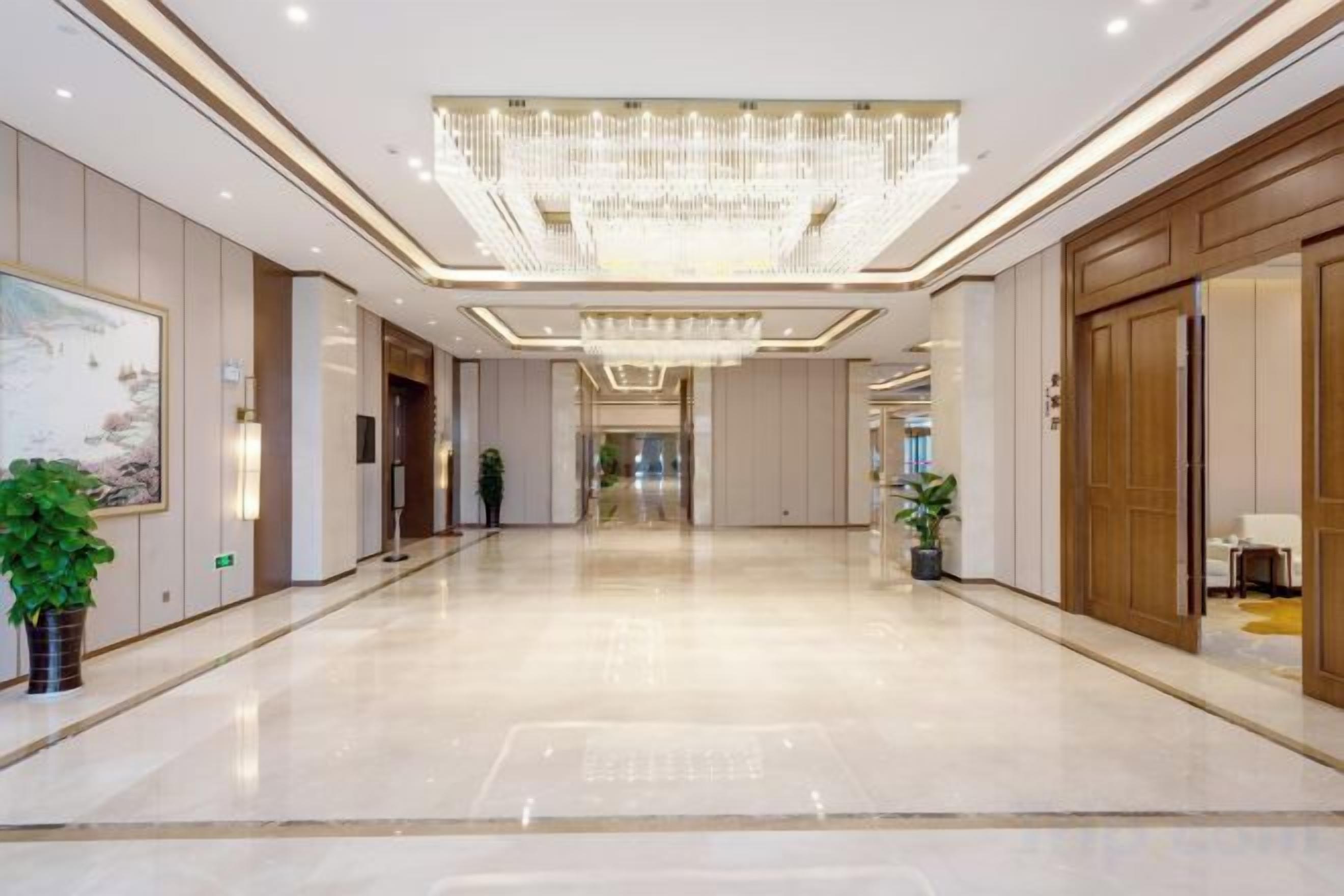 A spacious hotel lobby with a large chandelier, a reception desk, and a plant.