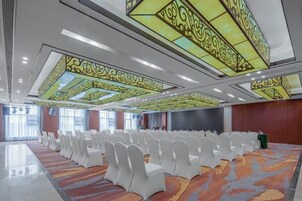 Un salón de conferencias con filas de sillas blancas, una alfombra estampada y una pantalla grande.
