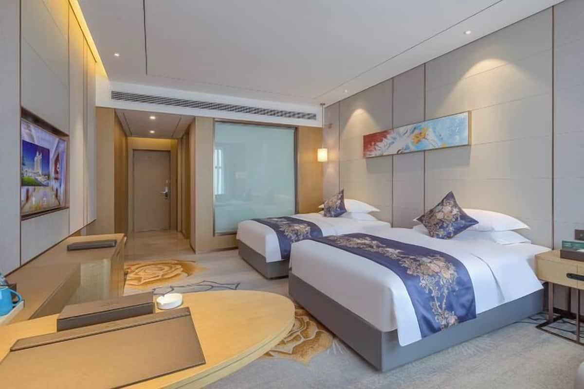 A modern hotel room with two beds, a desk, and a large window.