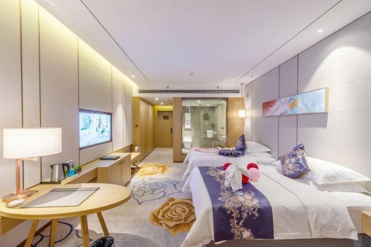 A hotel room with a bed, bedside table, lamp, TV, and a wall-mounted artwork.