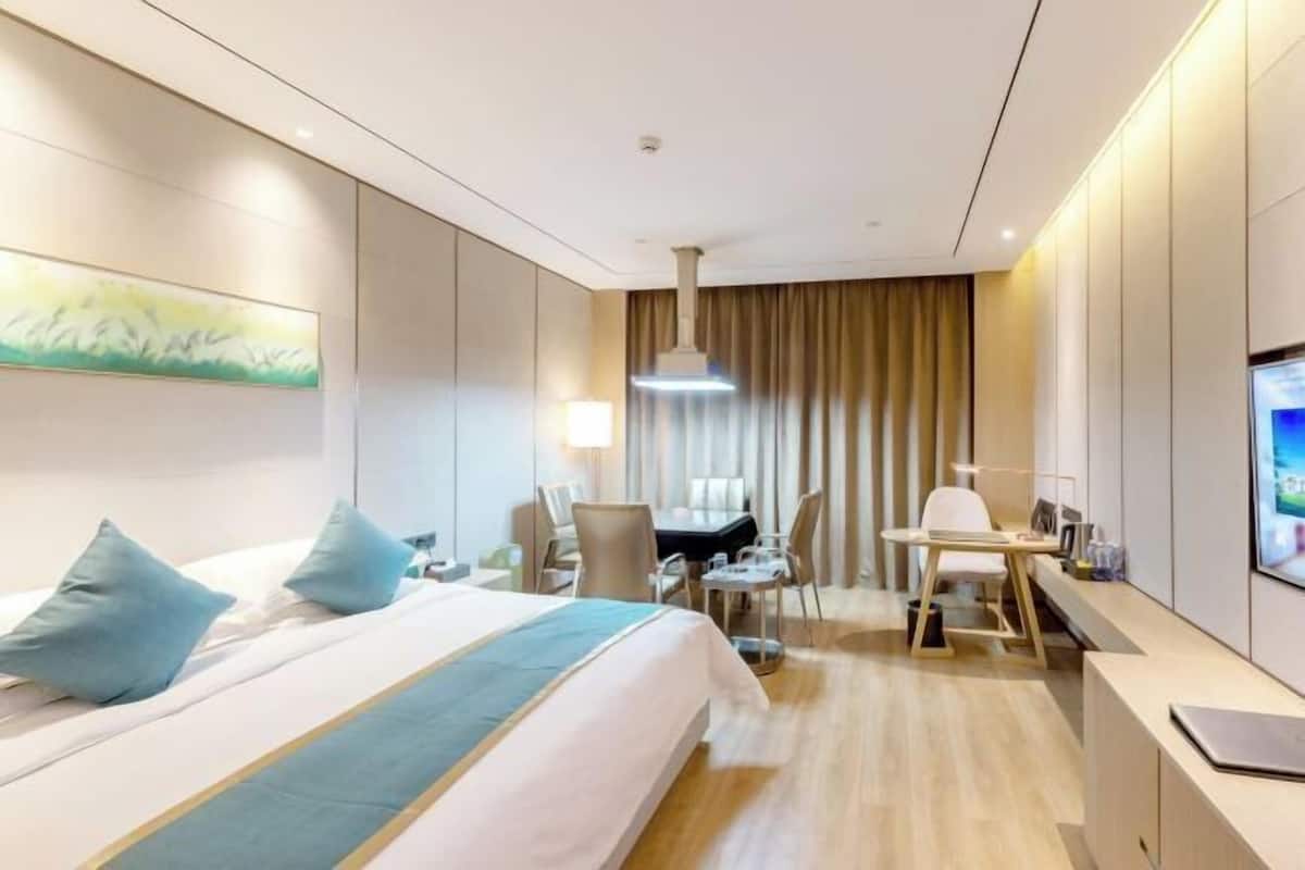 A hotel room with a large bed, a desk, a chair, and a television.
