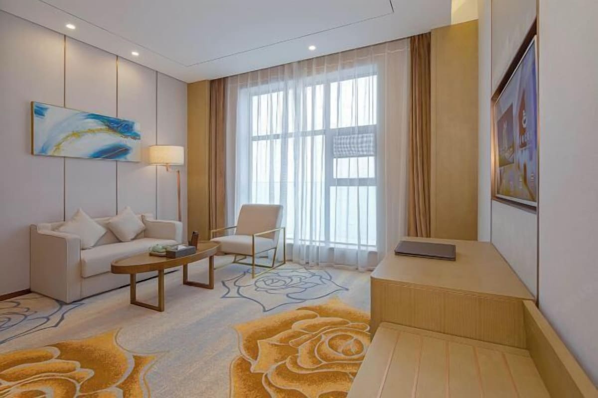 A hotel room with a sofa, armchair, coffee table, and a desk.