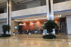 Um hall amplo com balcão de recepção, grandes vasos de plantas e design arquitetônico moderno.