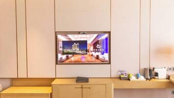 A hotel room with a mounted television displaying a cityscape, a small table with a book, and a counter with various items.