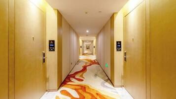A hotel hallway with a patterned carpet, doors, and a digital elevator display.