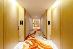 Ein Hotelgang mit Teppichmuster, Türen und einer digitalen Aufzugsanzeige.