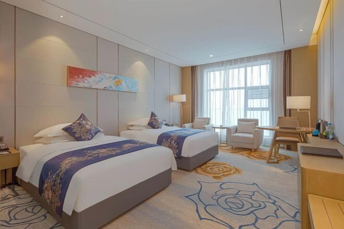 A hotel room with two beds, a desk, a chair, and a large window.