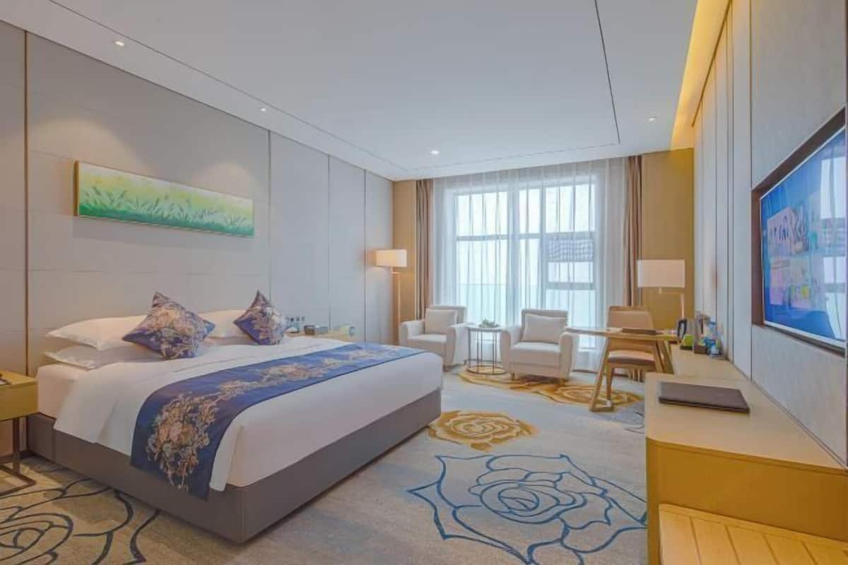A hotel room with a large bed, a desk with a laptop, a TV, and a seating area with chairs.