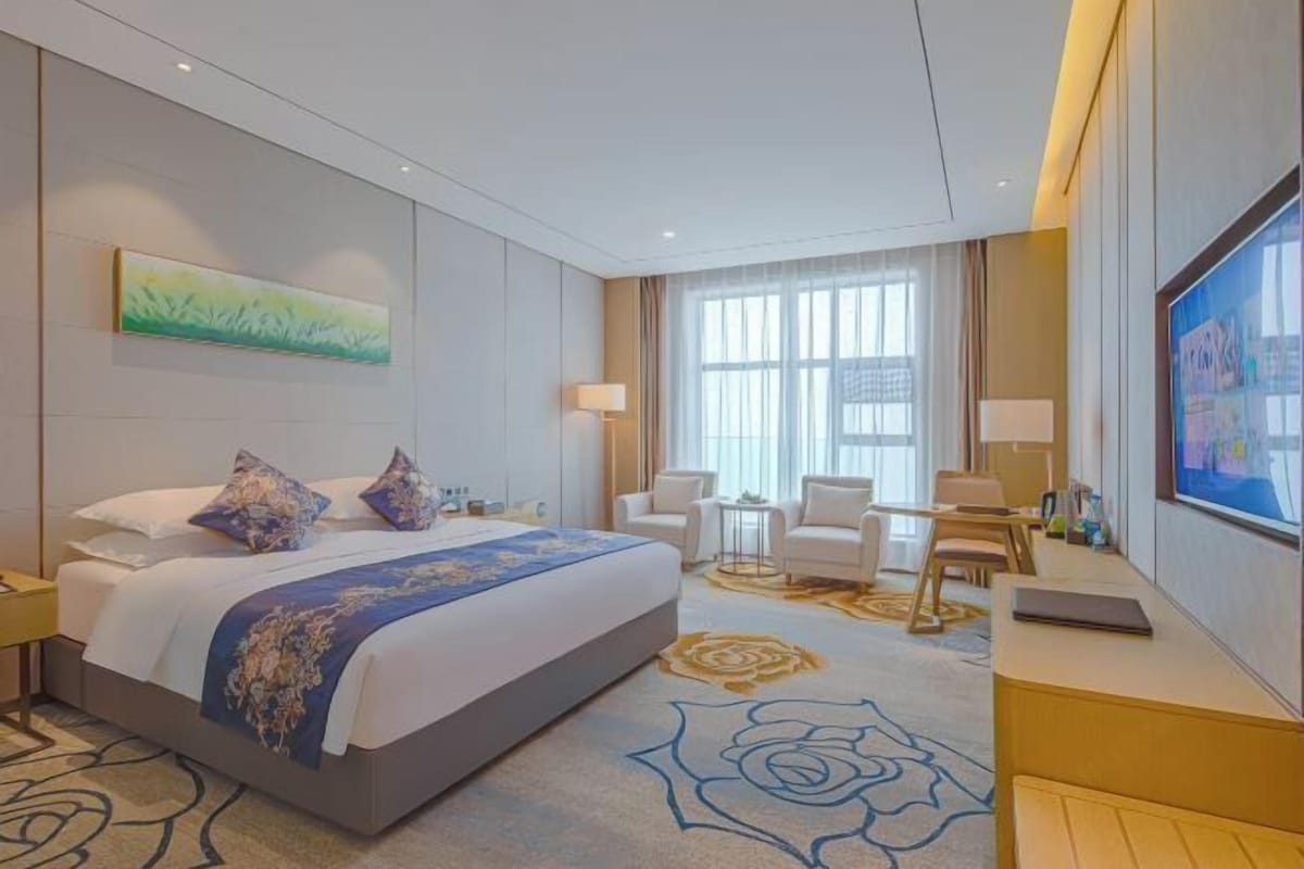 A hotel room with a large bed, a desk, a chair, a TV, and a window.