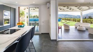 Une cuisine moderne dotée d’un grand îlot central, un coin repas offrant une vue sur une piscine et les montagnes, et une terrasse aménagée avec du mobilier d’extérieur.