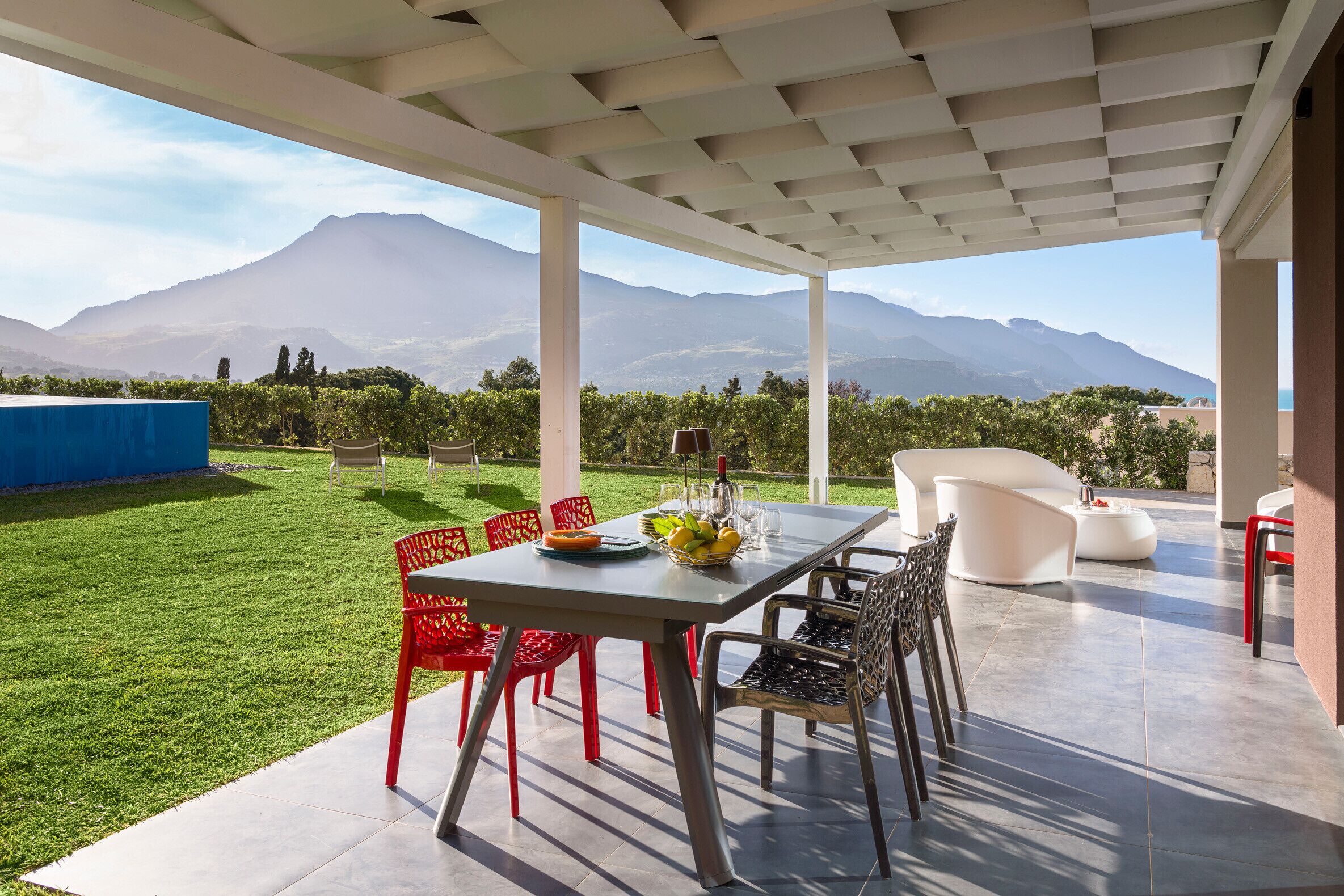 Une terrasse couverte avec une table dressée pour le repas, des chaises rouges et une vue sur les montagnes.