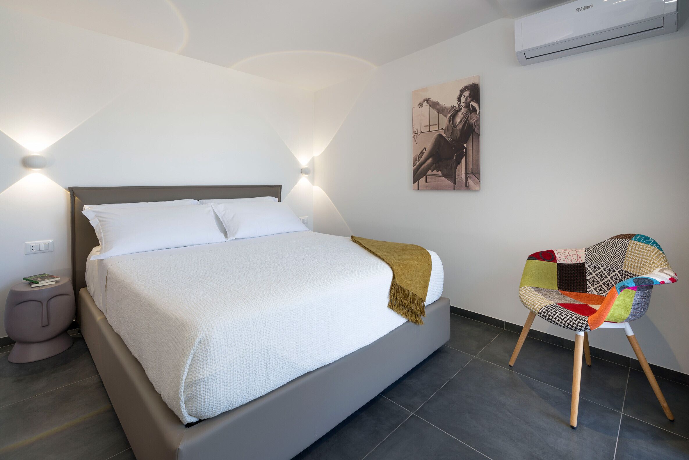 Une chambre moderne avec un grand lit, une table de chevet, une chaise et un climatiseur fixé au mur.