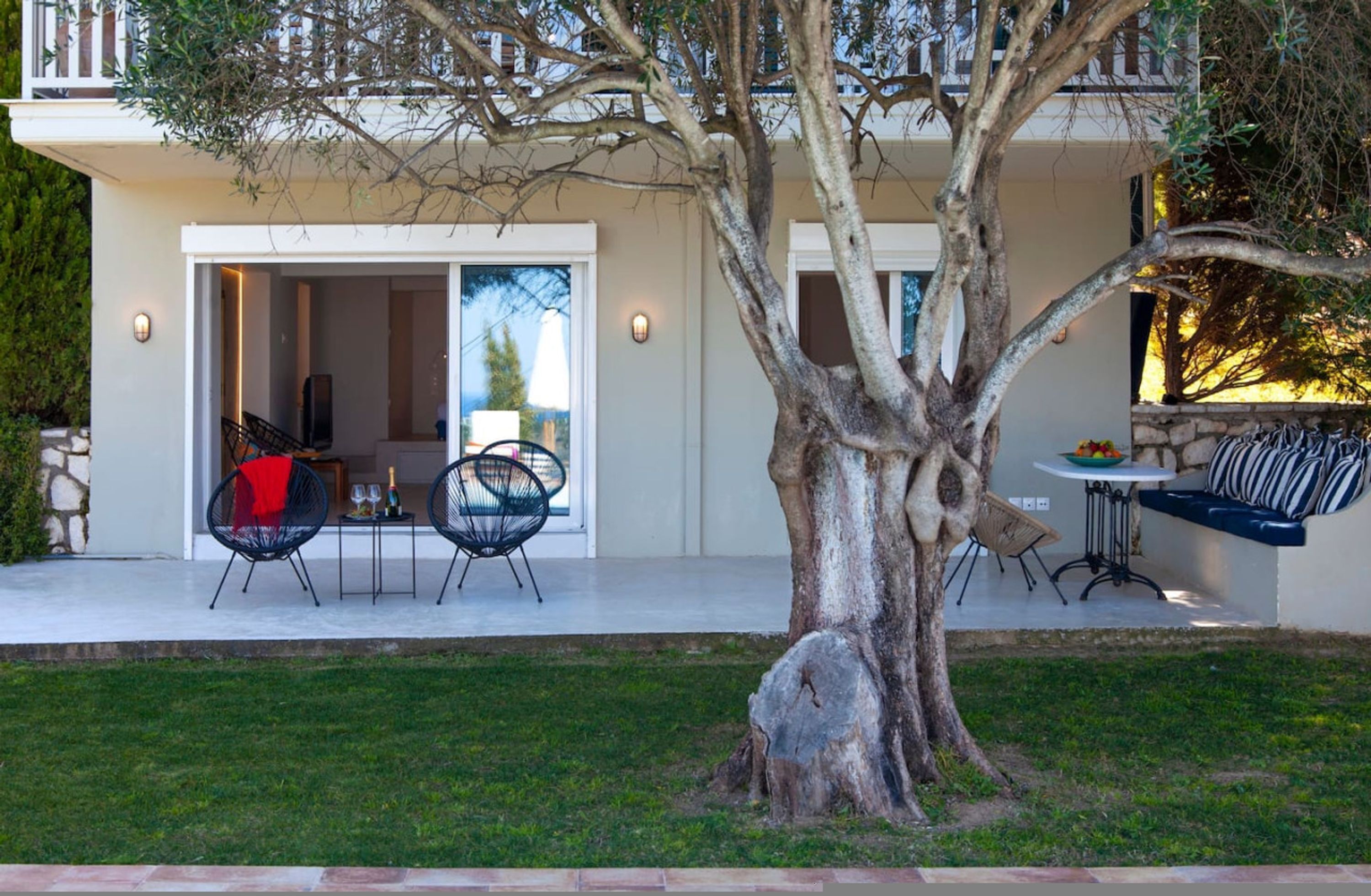 Una casa moderna con patio, arredi da esterno, un grande albero e un muro in pietra.