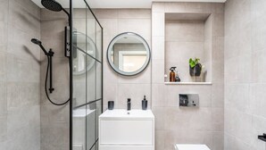 Un baño moderno con cabina de ducha de vidrio, un lavabo blanco con un espejo encima y un inodoro.
