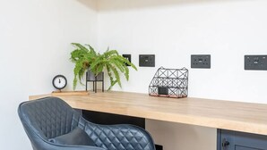 Un espacio de oficina moderno con un escritorio de madera, una silla de oficina negra, una planta en maceta y una estantería con una bicicleta y un objeto negro.