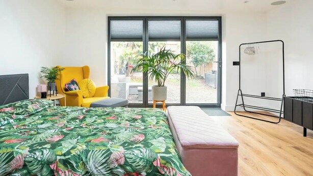 Un dormitorio moderno con una cama, un sillón amarillo, una pizarra y vistas al exterior.