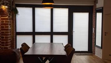 Un comedor con una mesa y sillas de madera, una lámpara colgante y una pared de ladrillo.