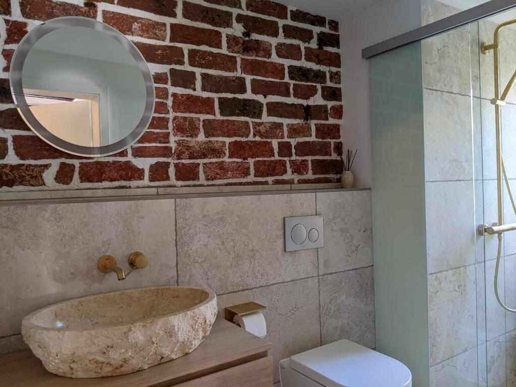 A bathroom with a stone sink, a round mirror, a toilet, and a glass shower enclosure.