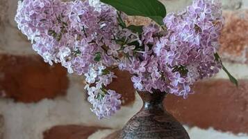 Eine Vase mit Fliederblüten auf einem Holztisch vor einer Backsteinwand.