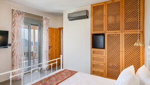A bedroom with a bed, a TV, an air conditioning unit, and a balcony with a table and chairs. - New Villa with spectacular 180° Sea View,Private Pool & BBQ,5 min from the Beach (Rethymnon)