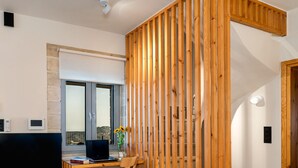 A modern living room with a wooden partition, a flat-screen TV, a laptop, and a desk with a chair. - New Villa with spectacular 180° Sea View,Private Pool & BBQ,5 min from the Beach (Rethymnon)