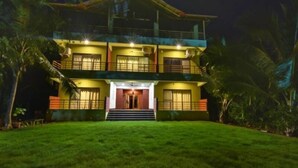 A two-story building with a well-lit entrance and a grassy front yard. - Laguna Beach Resort Murud (Dapoli)