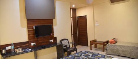 Quarto de hotel com cama, escrivaninha, cadeira, televisão e armário.