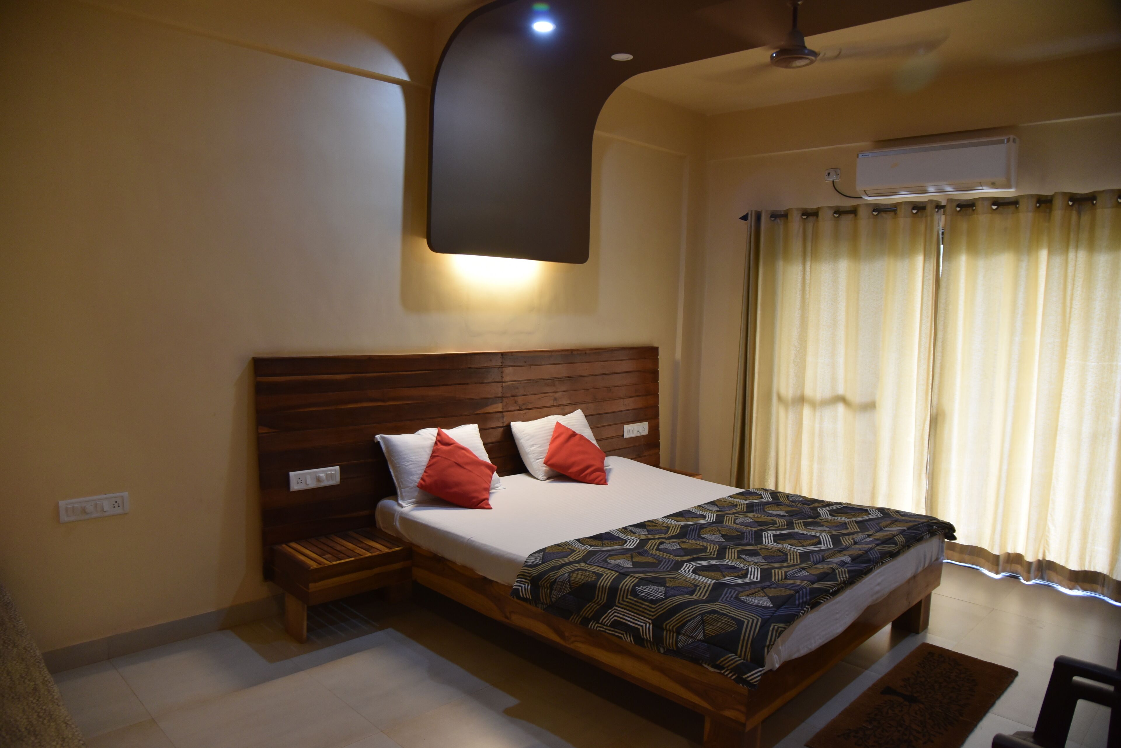 A bedroom with a wooden bed, a nightstand, a wall-mounted air conditioner, and a window with curtains.