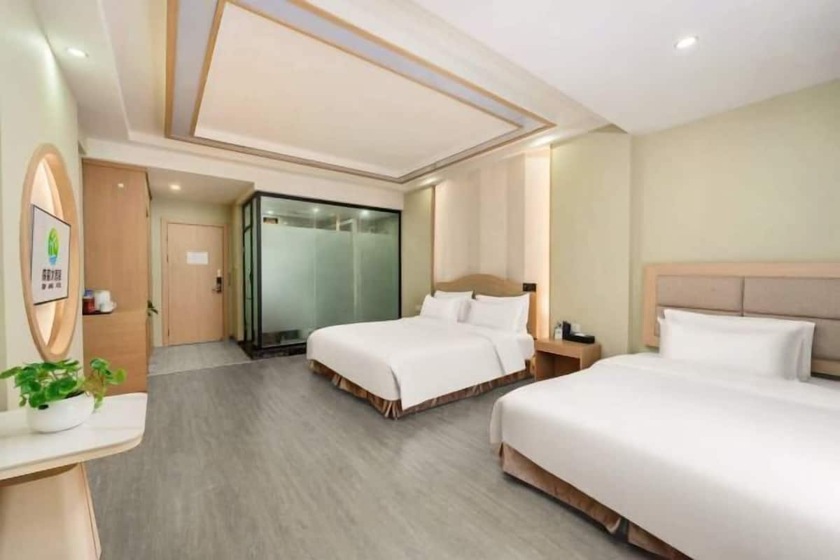 Une chambre d’hôtel avec deux lits, un bureau, un miroir, une plante et un espace douche.