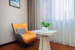 Une pièce avec un fauteuil orange au design moderne, une petite table blanche ornée d’une plante, un tableau encadré accroché au mur et des rideaux légers.