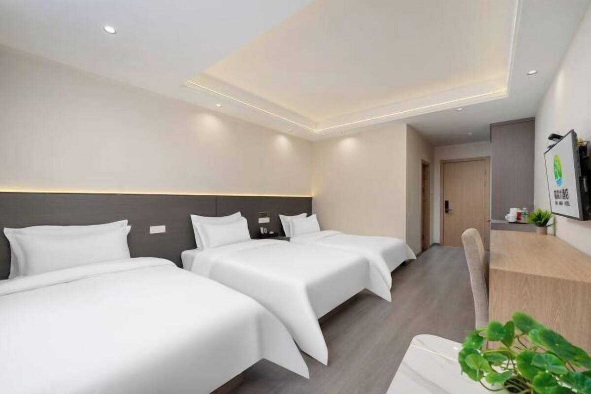 Une chambre d’hôtel avec trois lits, un bureau et une télévision.