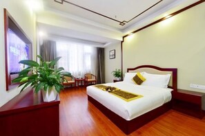 Une chambre d’hôtel avec un grand lit, un plancher en bois, un téléviseur fixé au mur et une plante en pot.