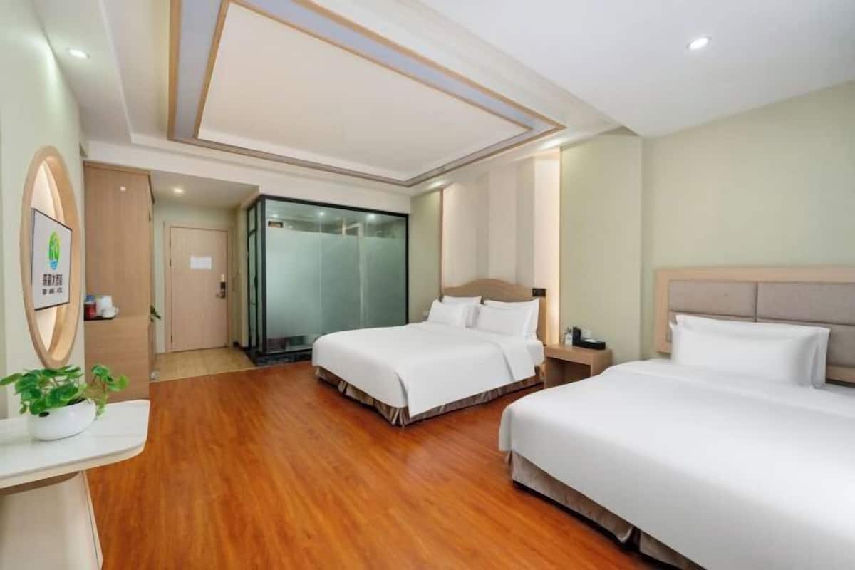 Une chambre d’hôtel avec deux lits, un plancher en bois, un espace douche et un comptoir de réception agrémenté d’une plante.