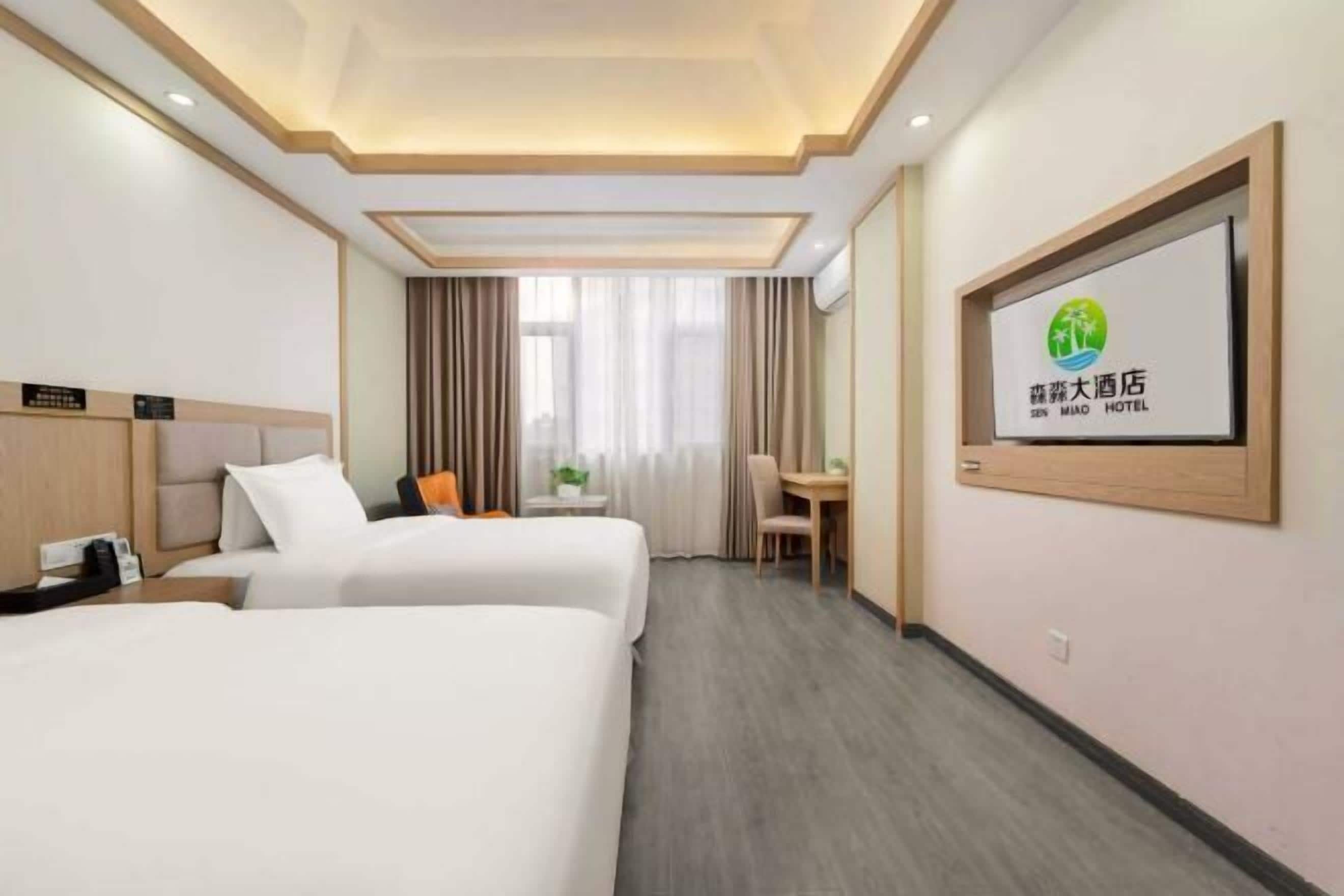 A hotel room with two beds, a desk, a chair, and a TV on the wall.