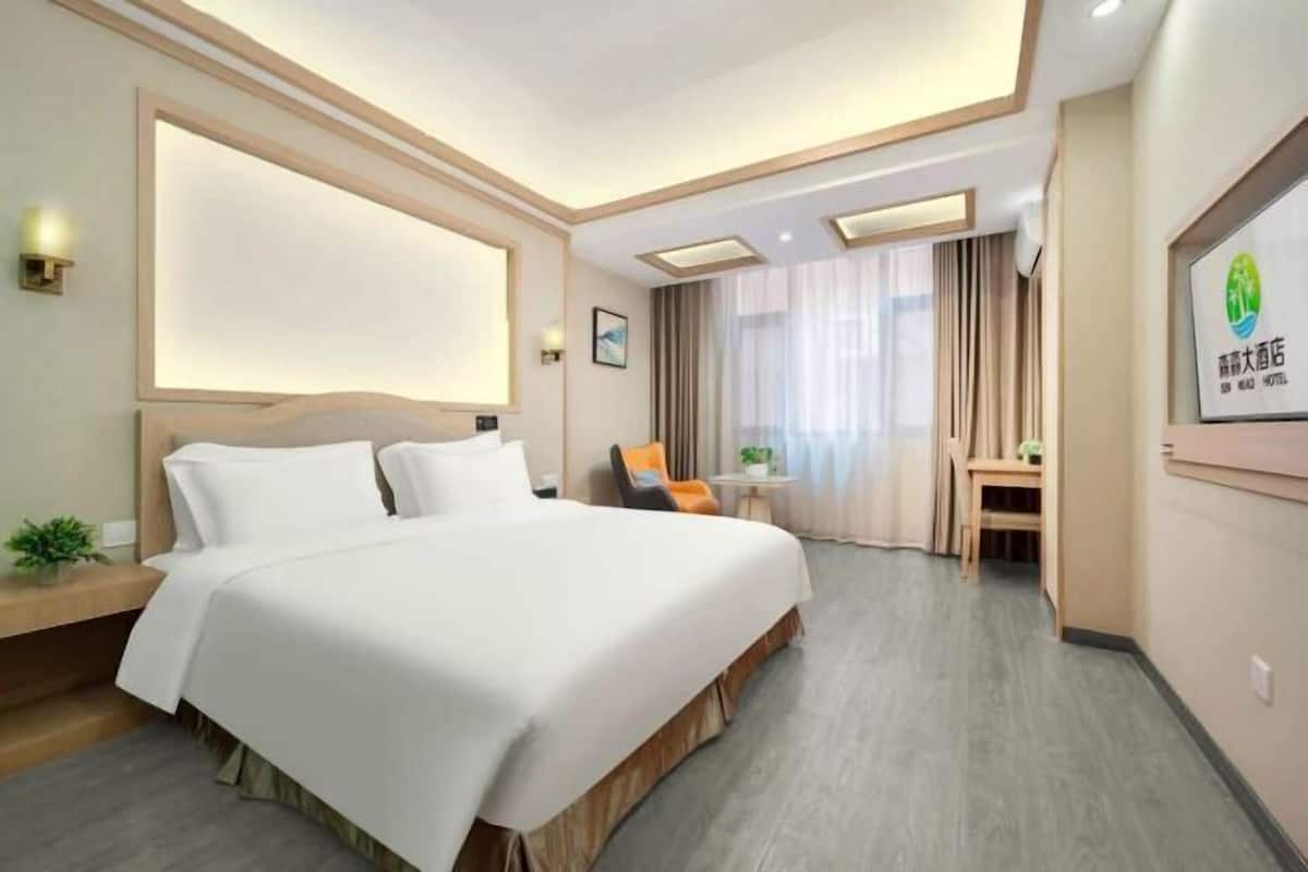 Une chambre d’hôtel avec un grand lit, un bureau, une chaise, une petite table avec une plante et un téléviseur fixé au mur.