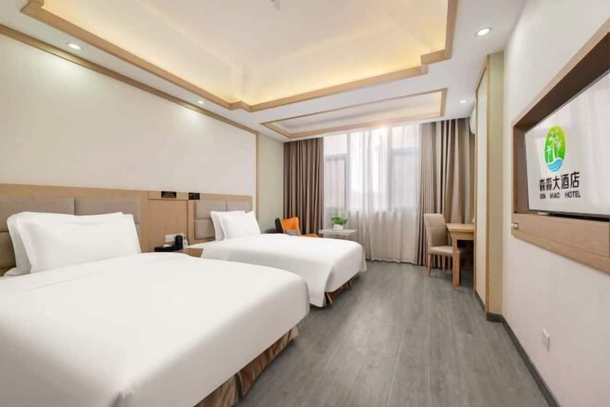 Une chambre d’hôtel avec deux lits, un bureau, une chaise et une grande fenêtre avec des rideaux.