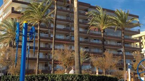 Ein Strandhotel mit mehreren Balkonen, Palmen und einem Sandstrand.
