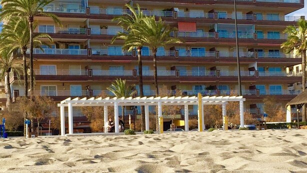 Ein Strandhotel mit mehreren Balkonen, Palmen und einer Sandstrandanlage.