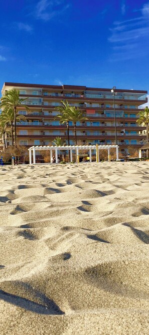 Un hotel sulla spiaggia con diversi balconi, palme e una zona di spiaggia sabbiosa.