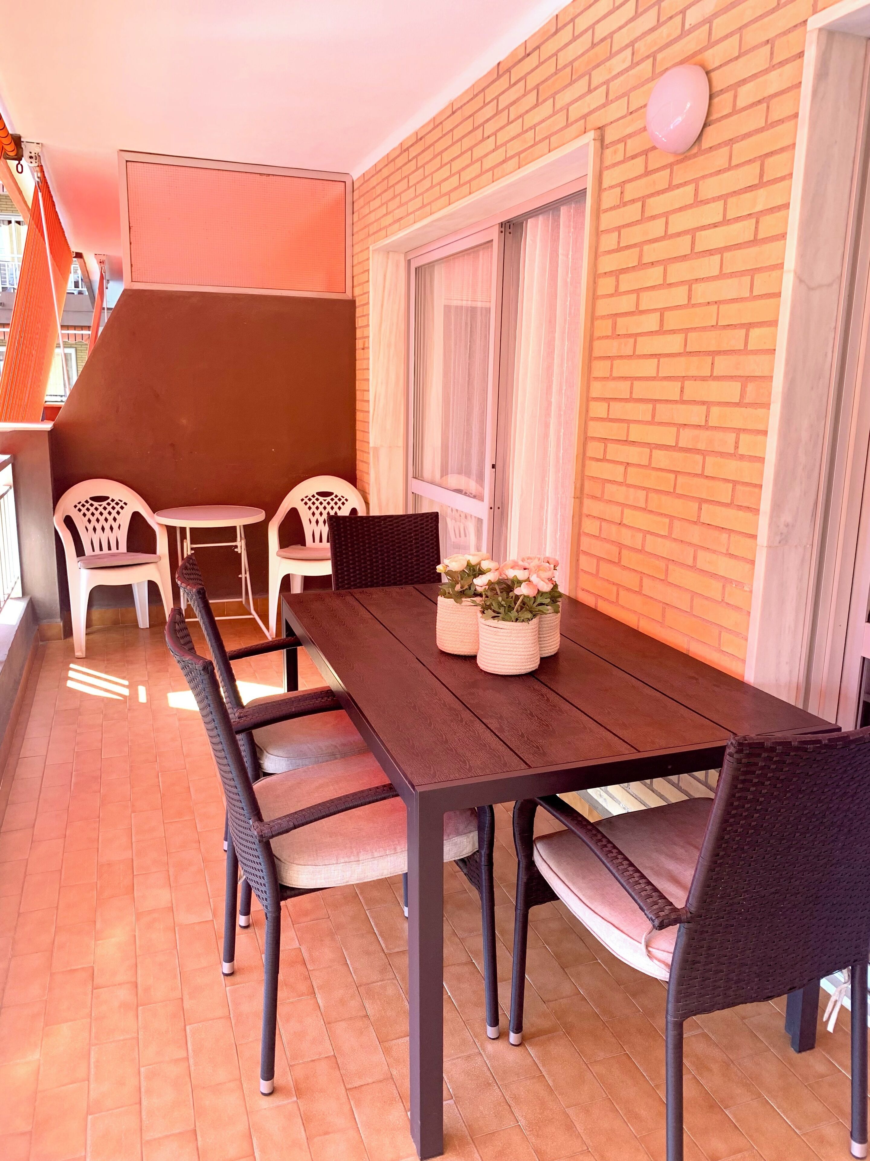 A patio with a wooden table and chairs, a window with curtains, and a brick wall.