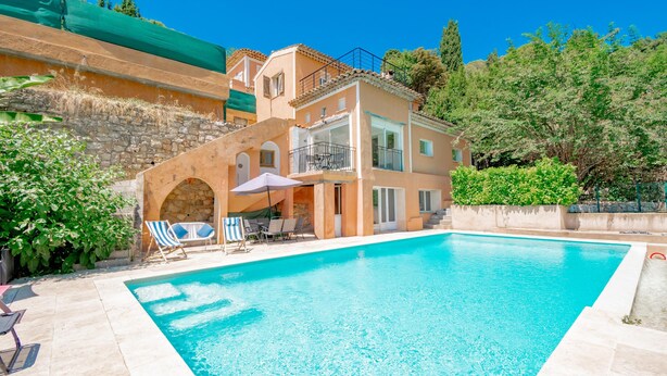 A two-story building with a swimming pool, outdoor seating, and a stone wall.