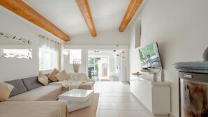 A modern living room with a sofa, coffee table, and TV. There is a fireplace and a dining area visible in the background.