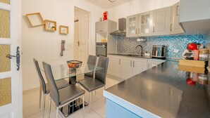 A modern kitchen with a glass dining table, white cabinets, and a blue-tiled backsplash.