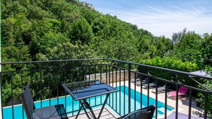 A pool area with a glass table and chairs, surrounded by lush greenery and a stone wall.